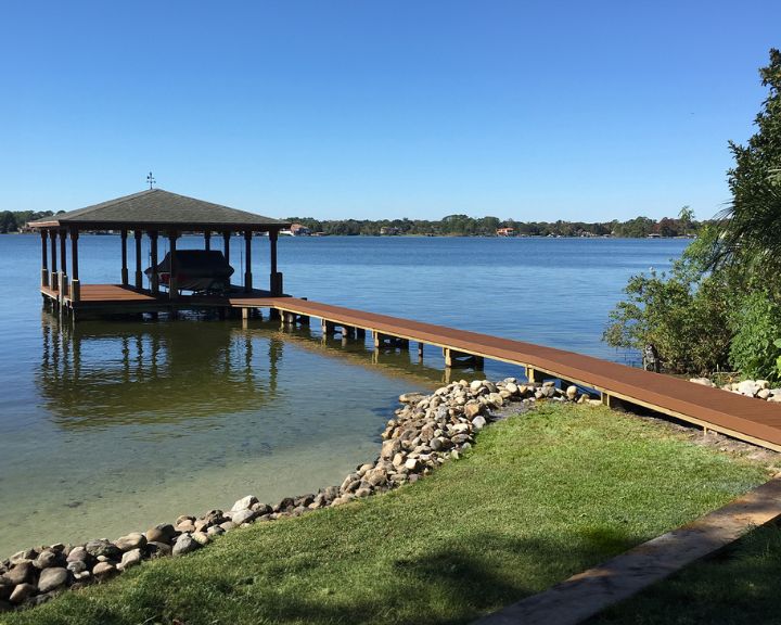Orlando Dock Builders proudly present a picturesque wooden dock adorning a serene lake wrapped in natural beauty. Nestled on the waterfront, this enchanting oasis features a charming gazebo, creating the perfect setting